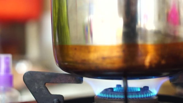 Blue gas stove flame being used to heat a copper and steel vessel