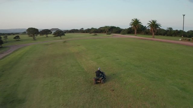 Aerial of man riding an ATV quad bike on grass, turns right and left