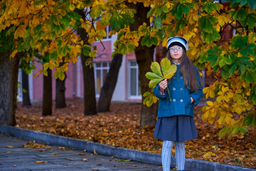 A teenager girl in glasses, a coat and a knitted hat on a walk in the autumn park.