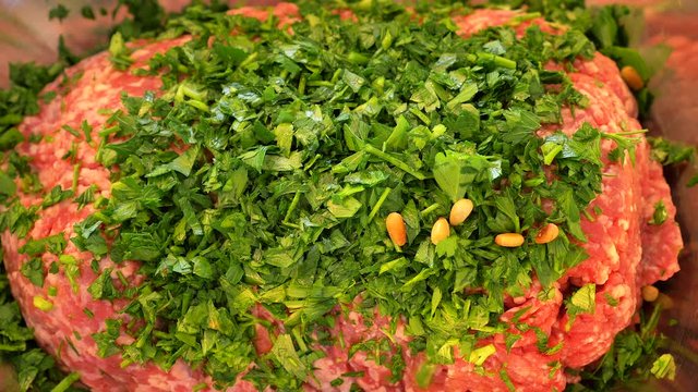 Adding Pine nuts to a large portion of finely ground meat with chopped Parsley, Base preparations for Kebabs, in slow motion.