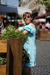 Young shorthair caucsian woman in blue dress and suglasses smiling while walking in sunny street