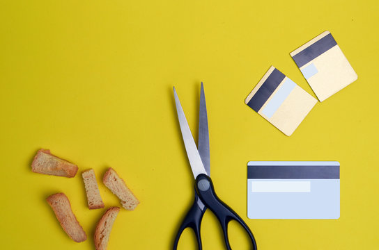 Scissors cut credit card on a green background with crumpled paper and breadcrumbs on a yellow background flat lay