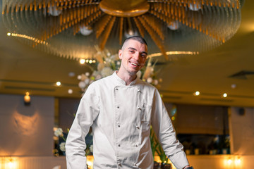 Young handsome cook chief posing in modern restaurant interior.