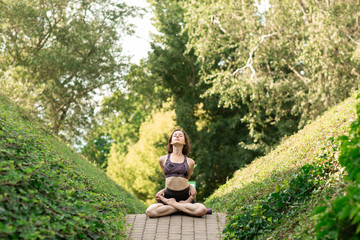 Fototapeta premium Young woman alone doing yoga on a park alley on a sunny summer day. Yoga concept