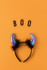 Halloween holiday flat lay. Party accessory, rim with devil horns and inscription Boo on orange background, copy space. Minimal style. Vertical. Trick-or-treat concept