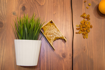 honey in combs next to raisins with green grass leaves on a wooden background