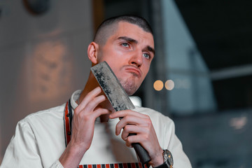 Young handsome cook chief holding knife and shaving his beard in modern restaurant interior.