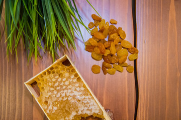 honey in combs next to raisins with green grass leaves on a wooden background