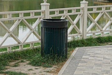 one black metal urn is standing by a white wooden fence on the shore near the water of a reservoir