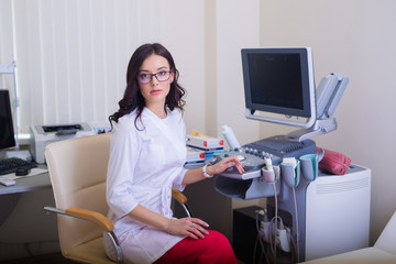 brunette girl in glasses. Doctor sits near the ultrasound diagnostic apparatus.