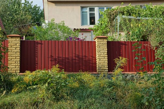 fence of red metal and brown bricks overgrown with green vegetation and grass