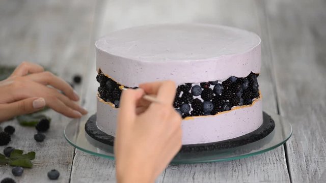 Step-by-step preparation of berries cake. The confectioner decorates a purple cake with gold food paint.