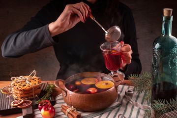 Female hands pour hot mulled wine from a copper pan into a glass.