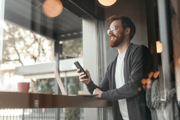Naklejka na ściany i meble Bearded freelancer using smartphone in cafe