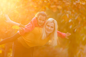 Mother giving daughter piggyback ride in autumn woodland