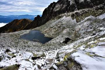 Fototapeta na wymiar Lake in the mountains, snow-covered stones, clouded sky, Tatra mountains.