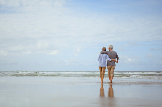 Senior Couples Walking On The Beach At Sunny Day, Plan Life Insurance With The Concept Of Happy Retirement.