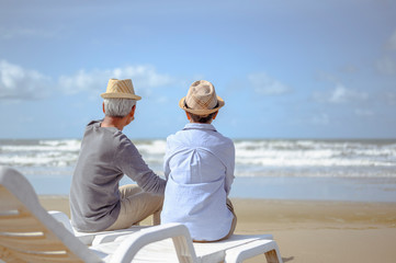 Senior couple sitting on chairs at the beach looking at the ocean on a good day and talking for to plan life insurance at retirement concept.