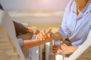Obraz premium Senior couple sitting hand in hand on chairs at the beach and looking at the ocean on a good day to plan life insurance at retirement concept.
