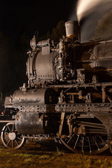 Fototapeta na wymiar Historic steam locomotive -wheels, rods, smokebox and steaming chimney close up at night illuminated