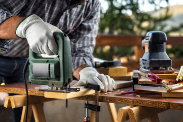 Adult carpenter craftsman wears protective leather gloves, with electric saw working on cutting a...