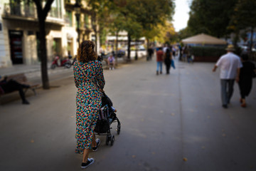 Mother with baby carriage on La Rambla street of Barcelona in summer, seen from behind. Shopping, parenthood and lifestyle concept.
