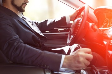 Businessman driving his car on background. Close-up human hand holding gear shift knob