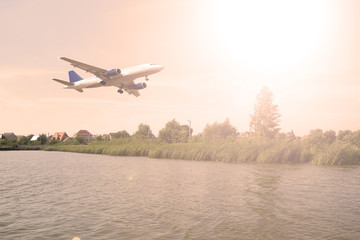 Large aircraft above the green plants and the lake. Sunset.