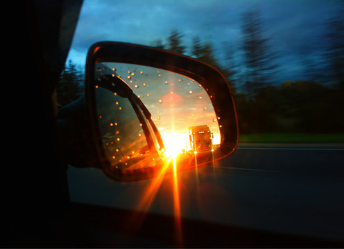 Car Mirror Of Rear View During Dramatic Sunset Background