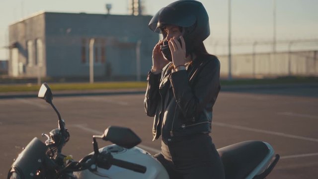 Beautiful young red-haired woman motorcyclist dancing on her custom bike in black motorcycle helmet