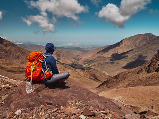 Tourist girl sits on the rock in High Atlas mountains and enjoyis view of the valley near Imlil in...