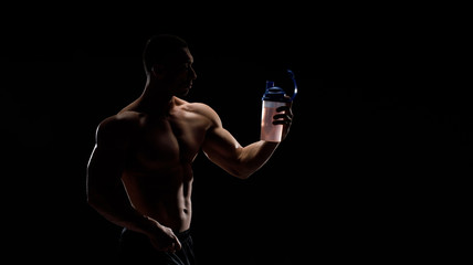 Model sports young man on dark background. Portrait of sporty strong muscle guy with protein drink in shaker. Sexy torso. Bodybuilding nutrition supplements, sport, workout, healthy lifestyle concept.