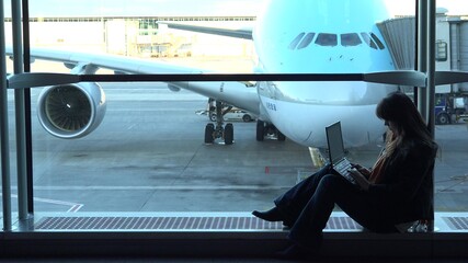 Beautiful woman looking at laptop in airport, sitting at big window, airplane