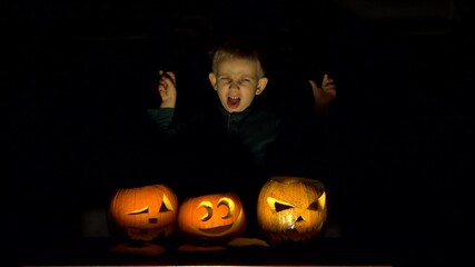 Amusing child playing as vampire close illuminated pumpkins, funniest Halloween