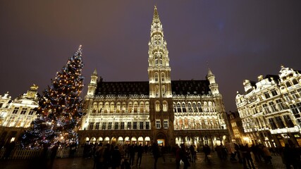 Fototapeta na wymiar Christmas tree and city hall of Brussels by night, people walk in Grand Place