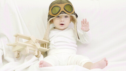 Funny baby with aviator cap playing with wooden plane toy
