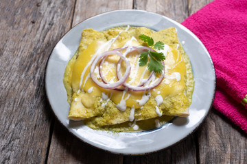 Mexican green enchiladas with melted cheese also called "suizas" on wooden background