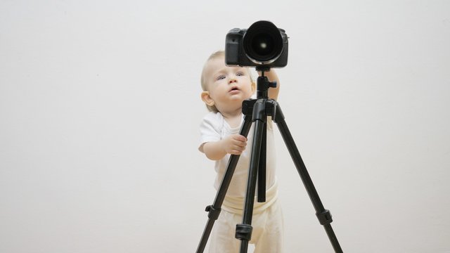 Adorable baby child playing with video camera on tripod