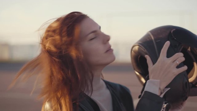beautiful young red-haired woman motorcyclist with black motorcycle helmet. Girl  biker undresses her helmet