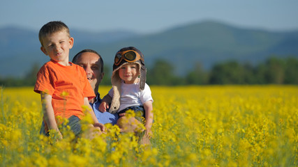 Father with two sons appearing from blossom rape field, have fun in nature