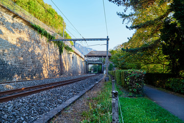 Railway at the foot of the mountain separated by a wall surrounded by greenery on a summer