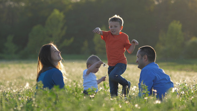 Happy Children And Parents Play With Dandelion Flower, Family Portrait At Sunset