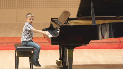 Funny child play careless at piano in concert hall, bad learning, boring