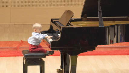 Little child playing at big piano in concert hall, early artistic education