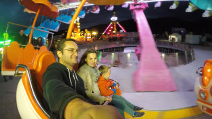 Mother, father, child in the spinning wheel at night in amusement park