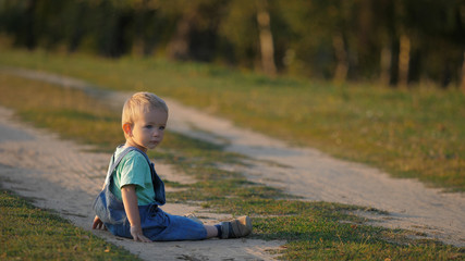 Lovely child sitting on rural pathway and playing with dust, kid look at camera
