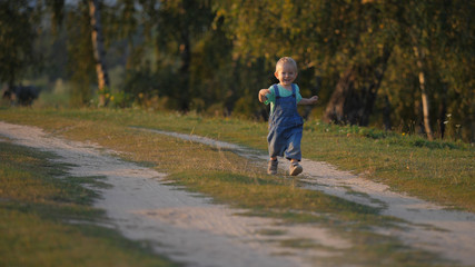 Fototapeta premium Amusing baby child run on countryside dusty road, childhood innocent happiness
