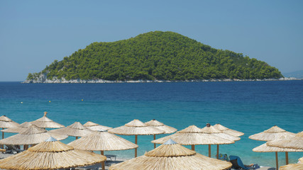 Beach straw umbrellas, turquoise sea and green island, perfect summer holiday
