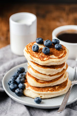 Breakfast pancakes with blueberries and cup of coffee on wooden table, vertical orientation