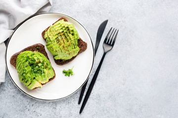 Sandwich with avocado and rye bread on white plate, gray concrete background with copy space. Healthy vegan vegetarian food
